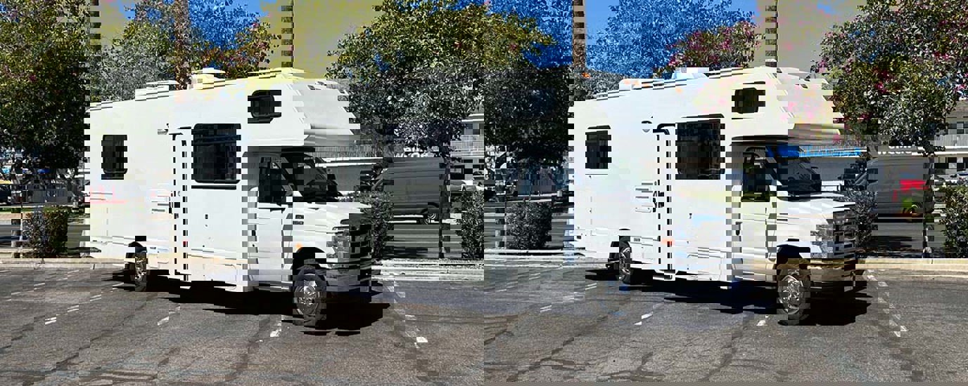 White RV with no Cruise America paint parked in parking lot.