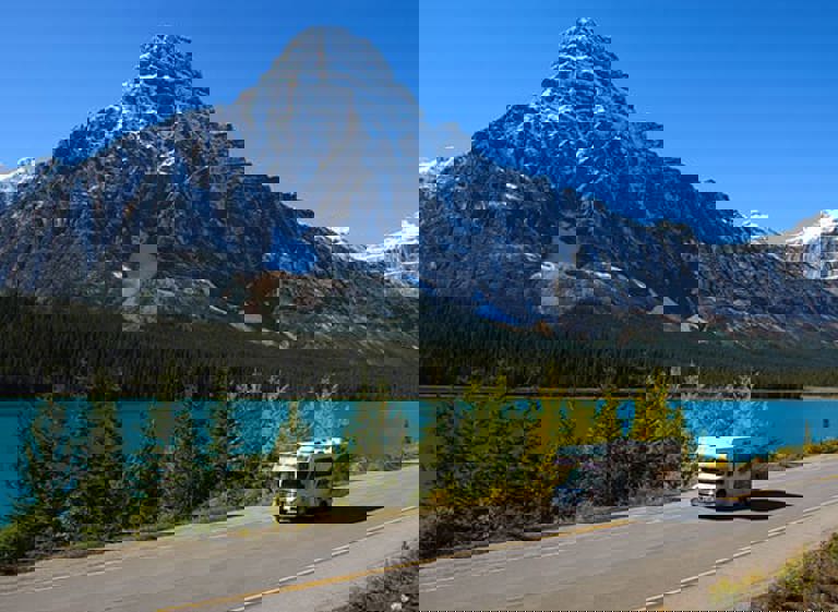 RV on road in front of blue lake and mountain.