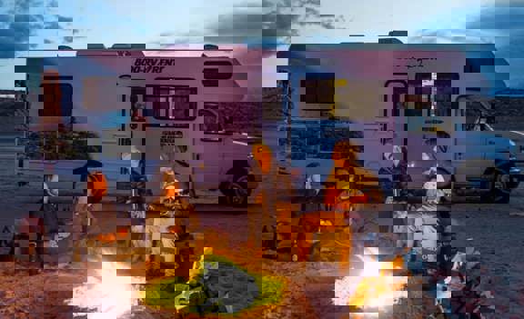 Group in front of campfire with Cruise America RV in background