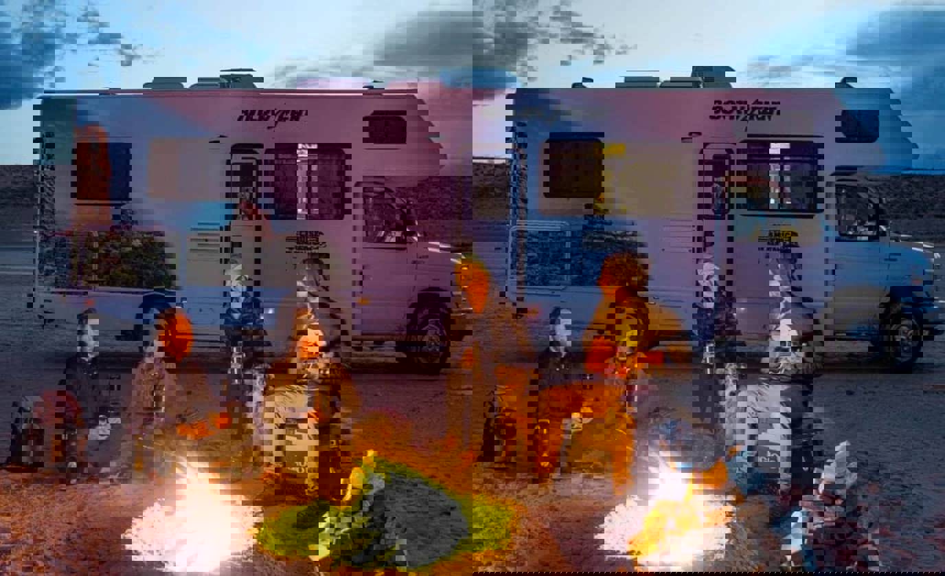 Group in front of campfire with Cruise America RV in background